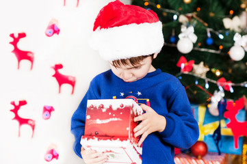 beautiful bright cheerful happy child boy looks into the gift presented at Christmas and New year emotionally surprised and considering what's inside