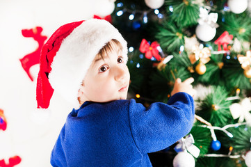 beautiful bright cheerful happy baby boy is very happy to dress up the Christmas tree for Christmas and New year emotionally surprised and hanging toys