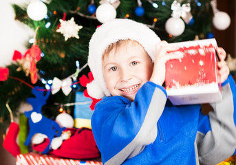 beautiful bright cheerful happy child boy is very happy gift presented for Christmas and New year emotionally surprised and cowardly gift near the ear listening to what's inside