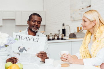 Obraz premium african american man reading newspaper while smiling mature woman drinking tea