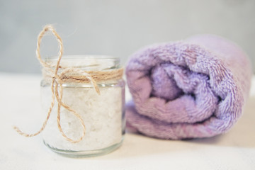 Natural herbal sea salt with aromatic herbs or botanicals - perfect for relaxation. Cosmetic jars and bottles with pink salt, fresh flowers, violet towel, wooden natural background.
