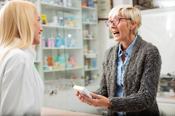 Angry mature female patient buying medications in a drugstore. Medicine, pharmaceutics, health care and people concept