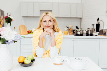 Fototapeta na wymiar smiling woman sitting at kitchen and drinking tea in morning