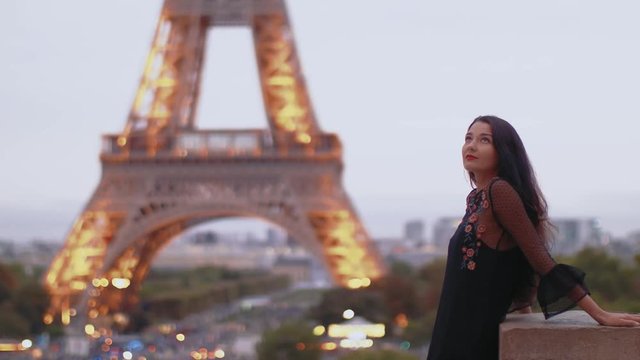 Elegant romantic Parisian woman in black sexy dress with flowers standing near the Eiffel tower in Paris, France on evening. Gorgeous mixed race Asian Caucasian girl enjoying traveling outdoors during