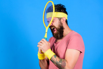 Tennis player retro fashion. Tennis sport and entertainment. Athlete hold tennis racket in hand on blue background. Tennis club concept. Man bearded hipster wear old school sport outfit with bandages