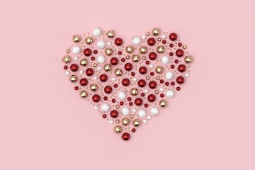 Minimal christmas background composition. Heart with scattered red, gold, white decoration balls and stars on pastel pink background. 3D rendering.