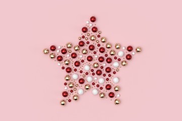 Minimal christmas background composition. Star with scattered red, gold, white decoration balls and stars on pastel pink background. 3D rendering.