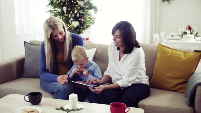 A small boy with mother and grandmother at home at Christmas time, using tablet.