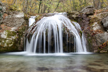 Waterfall in the yellow autumn forest near wet rocks