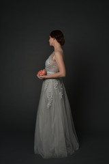 Naklejka premium full length portrait of brunette girl wearing long silver ball gown. standing pose on grey studio background.