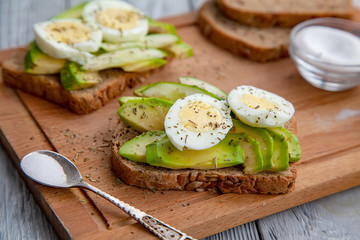 two avocado sandwiches with egg and spices on a wooden Board