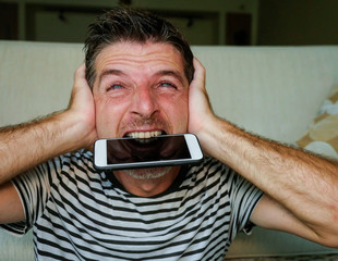 close up face portrait of young attractive and stressed man biting mobile phone desperate and...