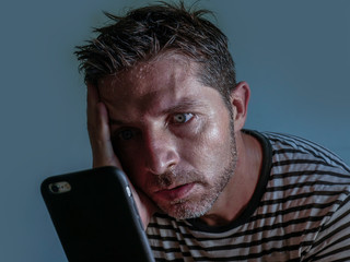 isolated close up face portrait of young attractive and stressed man using mobile phone feeling worried and frustrated looking anxious while reading bad news