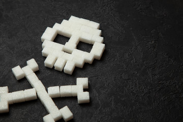 Skull from white sugar cubes on black background. Sugar kills and lot of fast ulevodov harmful to the body. Diabetes mellitus to death. Copy space for text