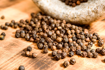 Tellicherry black peppercorns pouring out of a stone mortar onto a wooden cutting board.