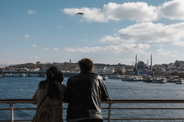 muslim couple hand in hand looking the amazing view of istanbul from the bridge - port with mosque in the background