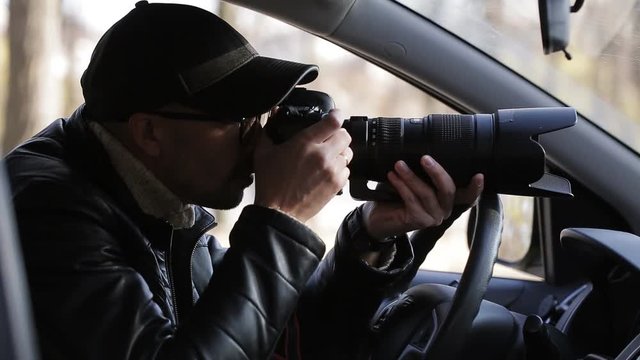 Spy, paparazzi or detective in the car, shooting on camera.