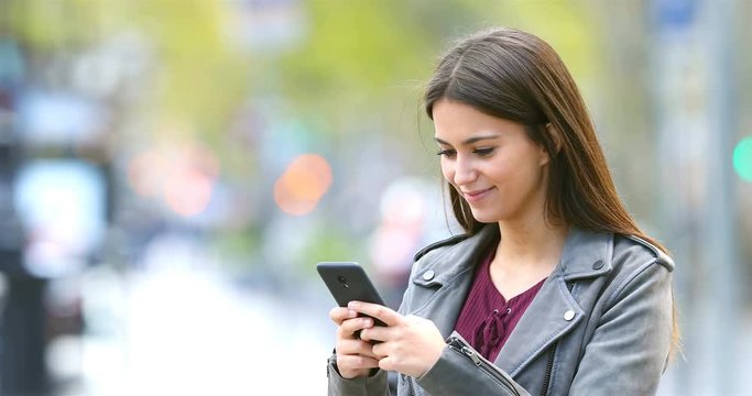Smiley fashion teenage girl texting on smart phone in the street