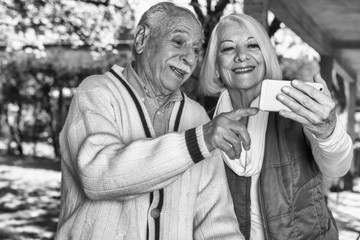 Obraz premium Elderly couple looking at the photos of their grandchildren on their cell phones