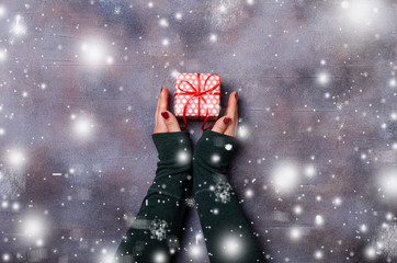 Female hands holding Christmas gift box on dark background. Flat lay, top view.