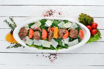Salad with goose liver, spinach, tomatoes and parmesan cheese. On a wooden background. Top view....