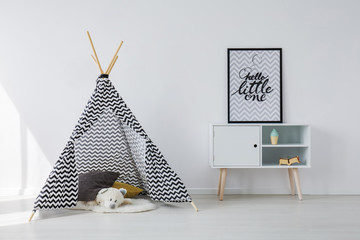 Patterned black and white scandinavian tent with grey and yellow pillows and white teddy bear next...