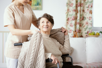 Nurse helping smiling elderly woman in the wheelchair during home visit