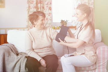 Obraz na płótnie Canvas Smiling doctor measuring pressure of happy senior woman at home