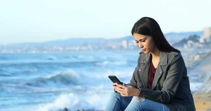 Relaxed teen checking smart phone and looking at horizon on the beach