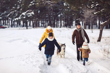 Fototapeta na wymiar Happy young caucasian family plays with a dog in winter in a pine forest