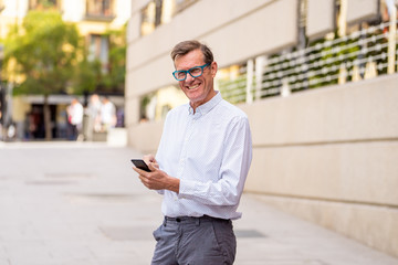 Smiling attractive stylish mature man using smart phone in urban outdoors city