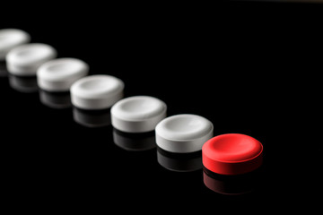 Behind the red pill are lined up white pills. One red and many white pills on a black background. With blur in perspective. Concept on leadership and features. From left to right. Top down.