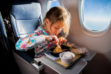 Child eating pancakes in airplane. Little girl having breakfast while flying in aircraft. Blue sky...