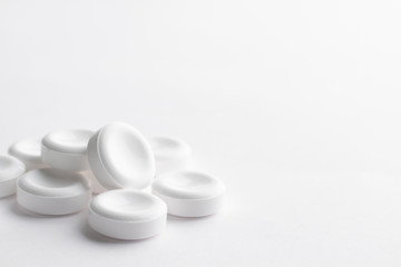 A handful of large white tablets lies on a white background. Concept on the topic of medicines with space for text. Excellent light minimalistic background in high key.