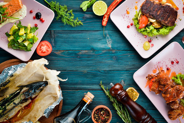 Background of food and dishes. Meat and fish dishes, and salad. On a wooden background. Top view. Free space for your text.