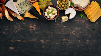 Set cheeses. Suluguni, blue cheese, mozzarella, maasdam, brie cheese. Top view. On a black wooden background. Free copy space.