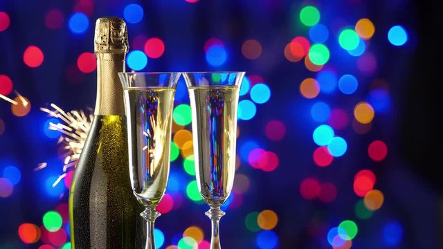 Still-life with a bottle of champagne and glasses. Behind the flashing lights and sparklers of the Christmas holiday.  4K video.