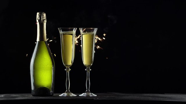 Still-life with a bottle of champagne and glasses. Sparklers on a black background. 4K video.