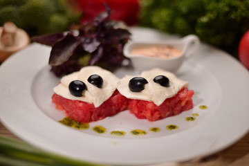 tomato carpaccio with mozzarella and and olives on a white plate