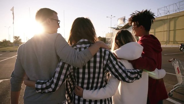 Group of four young multirace friends laughing while walking outdoors. Young men and women enjoying a summer day at parking zone near the mall. Rare view