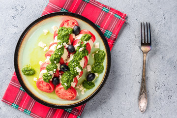 Tomato and mozzarella caprese salad and pesto sauce with olives on gray table