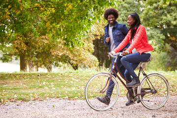 Black man running in a park beside his girlfriend, who is riding a bike, side view