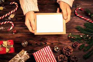 Female hands writing letter to Santa Claus on wooden background with christmas gifts and decoration...