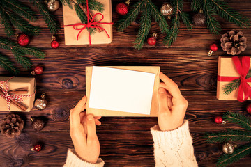 Female hands writing letter to Santa Claus on wooden background with christmas gifts and decoration...