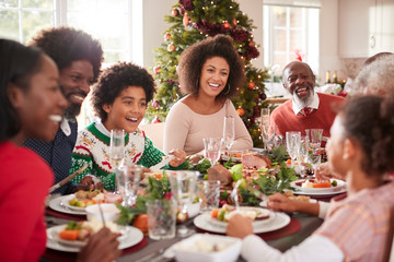 Happy multi generation mixed race family sitting at their Christmas dinner table eating and talking, selective focus