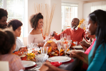Multi generation mixed race family holding hands and saying grace before eating at their Thanksgiving dinner table, selective focus
