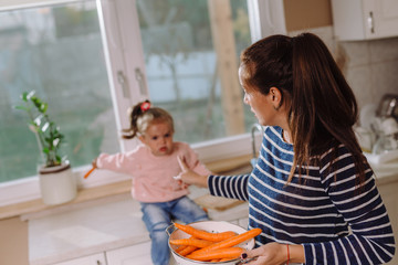 Mother and daughter in kitchen. Mother holding carrots