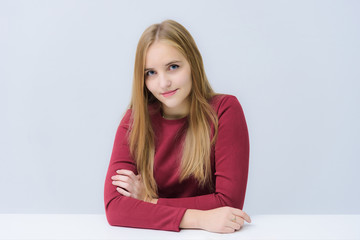Fototapeta premium Concept portrait of a beautiful blonde girl on a white background smiling, talking while sitting at the table.