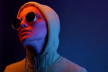 Neon portrait of young woman in round sunglasses and hoodie. Studio shot