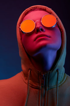 Neon portrait of young woman in round sunglasses and hoodie. Studio shot